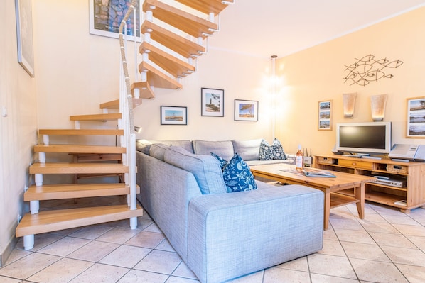 A living room with a staircase, a sofa, a coffee table, a TV, and wall-mounted picture frames.