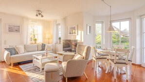 Ein modernes Wohnzimmer mit Sofa, Couchtisch, Sesseln und einem Esstisch.