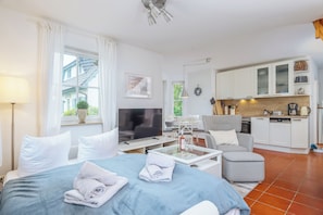 A modern hotel room with a bed, a TV, a dining area, and a kitchen.