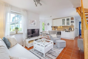 A modern living room with a TV, sofa, and coffee table, a kitchen with white cabinets, and a dining area.