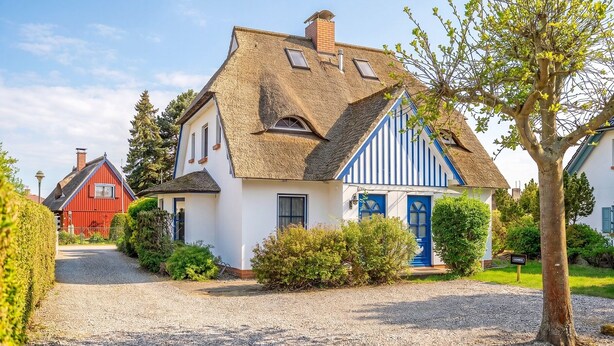Ein Haus mit Strohdach, blauer Tür und Auffahrt mit Kies.