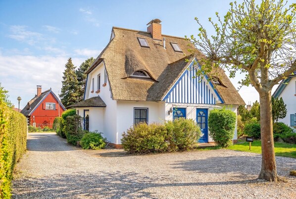 A house with a thatched roof, a blue door, and a gravel driveway.