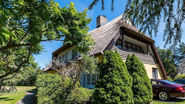 A traditional house with a steeply pitched roof, surrounded by lush greenery and a bicycle.