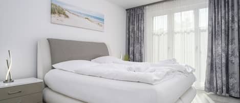 A modern bedroom with a large bed, a bedside table, a nightstand, and a painting of a beach scene.