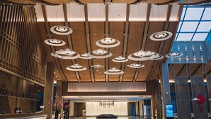 A spacious lobby with a modern design, featuring a central reception area, a large open space, and a high ceiling with circular light fixtures.