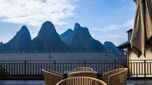 A terrace with wicker chairs and a wooden table, overlooking a mountainous landscape.