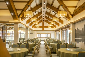 A conference room with round tables and chairs, wooden beams on the ceiling, and large windows.