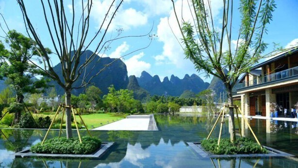A serene indoor pool with clear reflections, surrounded by lush greenery and mountains in the background.