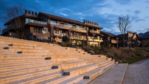 A multi-story hotel with a stone staircase leading to the entrance, surrounded by trees and a clear sky.