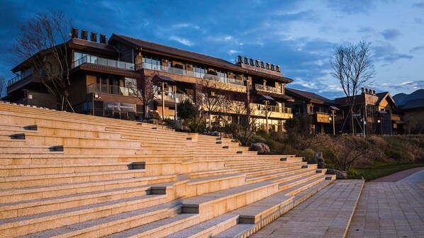 A multi-story hotel with a stone staircase leading to the entrance, surrounded by trees and a clear sky.