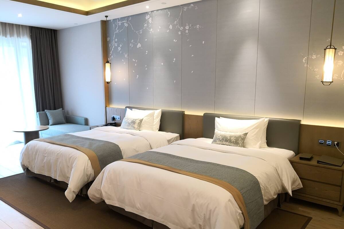 Hotelkamer met twee bedden, een bank, een bureau en een groot raam met gordijnen.