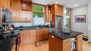 A modern kitchen with wooden cabinets, stainless steel appliances, and a black countertop. - LOVELY VIEWS from this beautiful modern townhome in DT Hood River!! (Hood River)