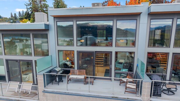 A modern multi-story building with large windows, a balcony with seating, and a view of a mountainous landscape. - LOVELY VIEWS from this beautiful modern townhome in DT Hood River!! (Hood River)