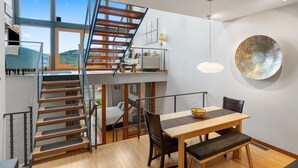 A modern interior with a staircase leading to a loft bedroom, a dining area with a table and chairs, and a large window offering a view of the outdoors. - LOVELY VIEWS from this beautiful modern townhome in DT Hood River!! (Hood River)