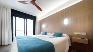 Habitación de hotel con una cama grande, dos mesitas de noche, un ventilador de techo y vistas al exterior.