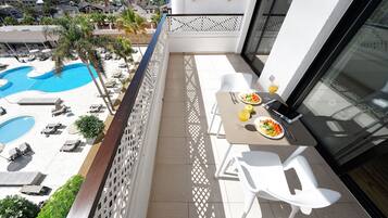 Een balkon met een eettafel, stoelen en uitzicht op een zwembad en hotelgebouwen.