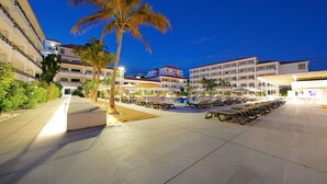 Un patio de hotel con piscina, tumbonas y palmeras.