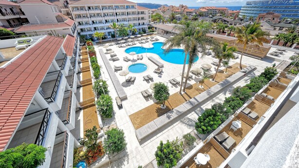 Un resort con un amplio espacio de piscina, numerosas tumbonas y vistas de los edificios y montañas circundantes.
