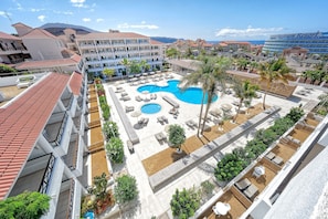 Ein Resort mit großzügigem Poolbereich, zahlreichen Liegestühlen und Blick auf die umliegenden Gebäude und Berge.