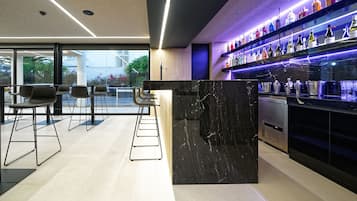 Zona de bar moderna con mostrador de mármol, taburetes y estantes llenos de botellas de licores.