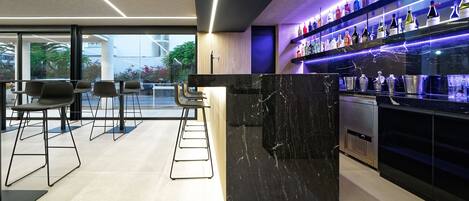 A modern bar area with a marble counter, bar stools, and shelves of liquor bottles.