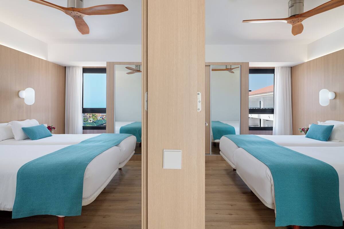 A mirrored room with two beds, wooden floors, ceiling fans, and a balcony view.