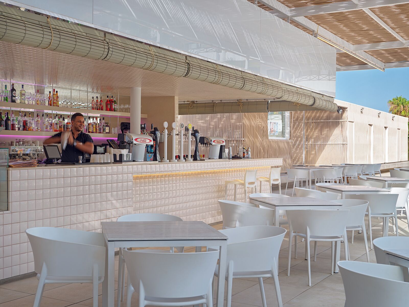 Un espace bar extérieur doté d’un comptoir carrelé, de chaises et de tables blanches.