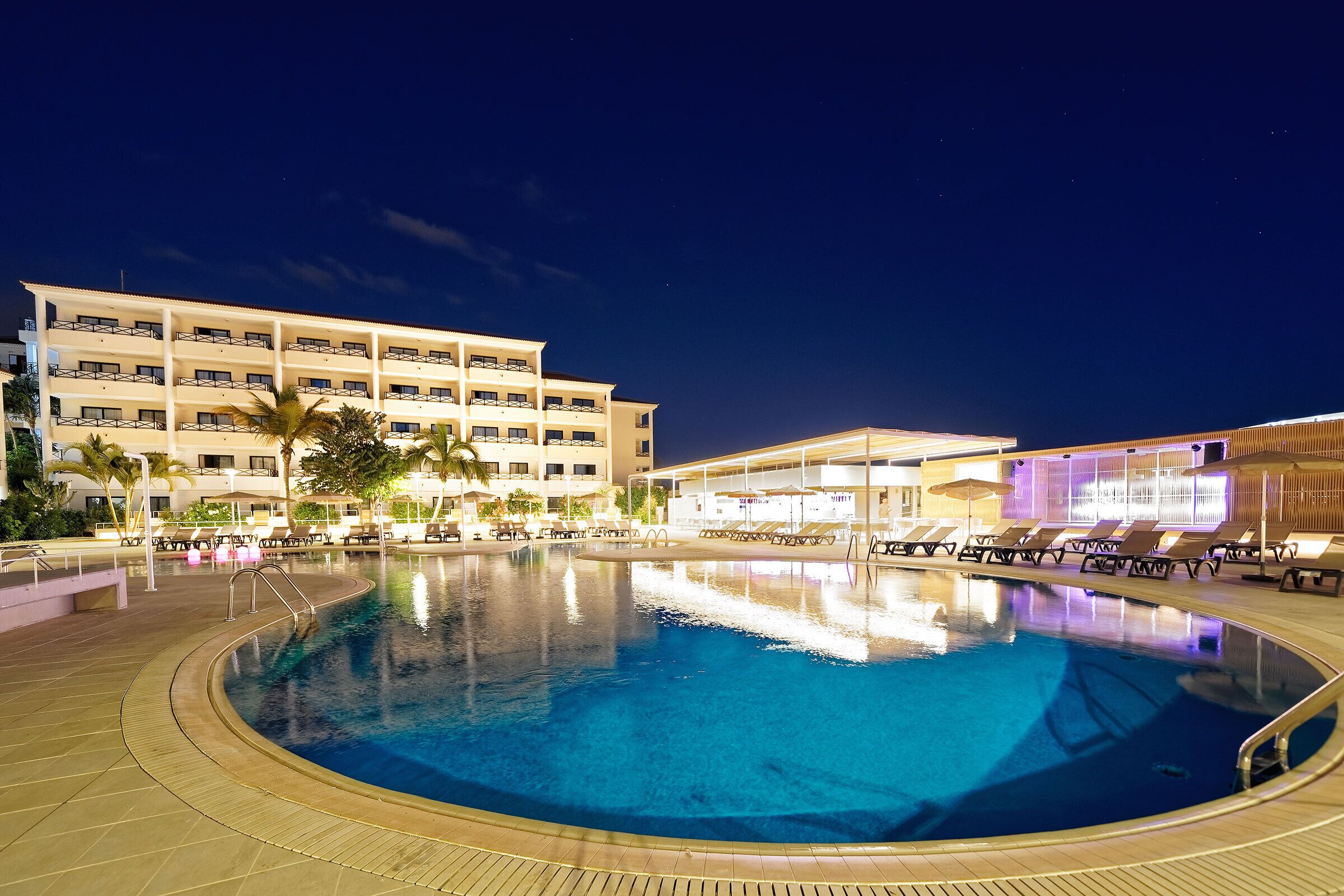 A hotel with a swimming pool, multiple floors, and outdoor seating areas.