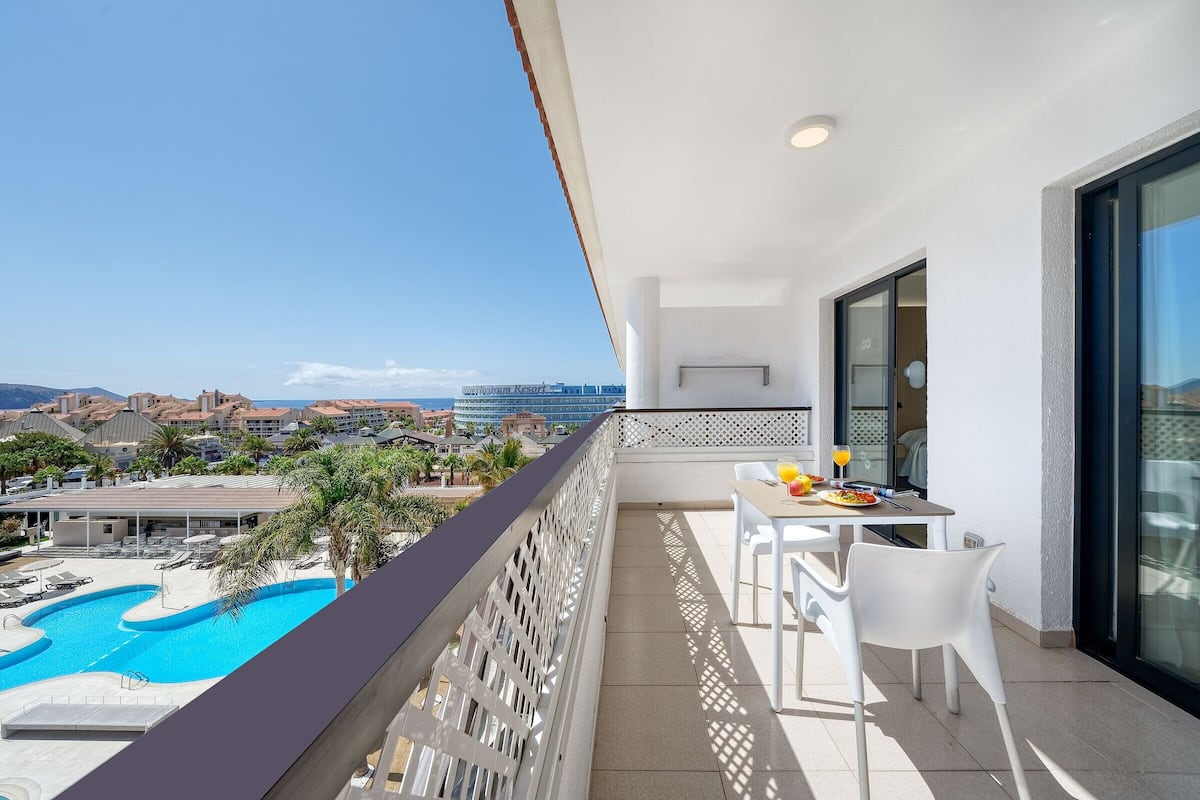 A balcony with a pool view, white furniture, and a dining area with a table and chairs.