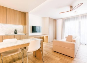 Un salon moderne comprenant un canapé, une table à manger avec des chaises, un téléviseur fixé au mur et un ventilateur de plafond.