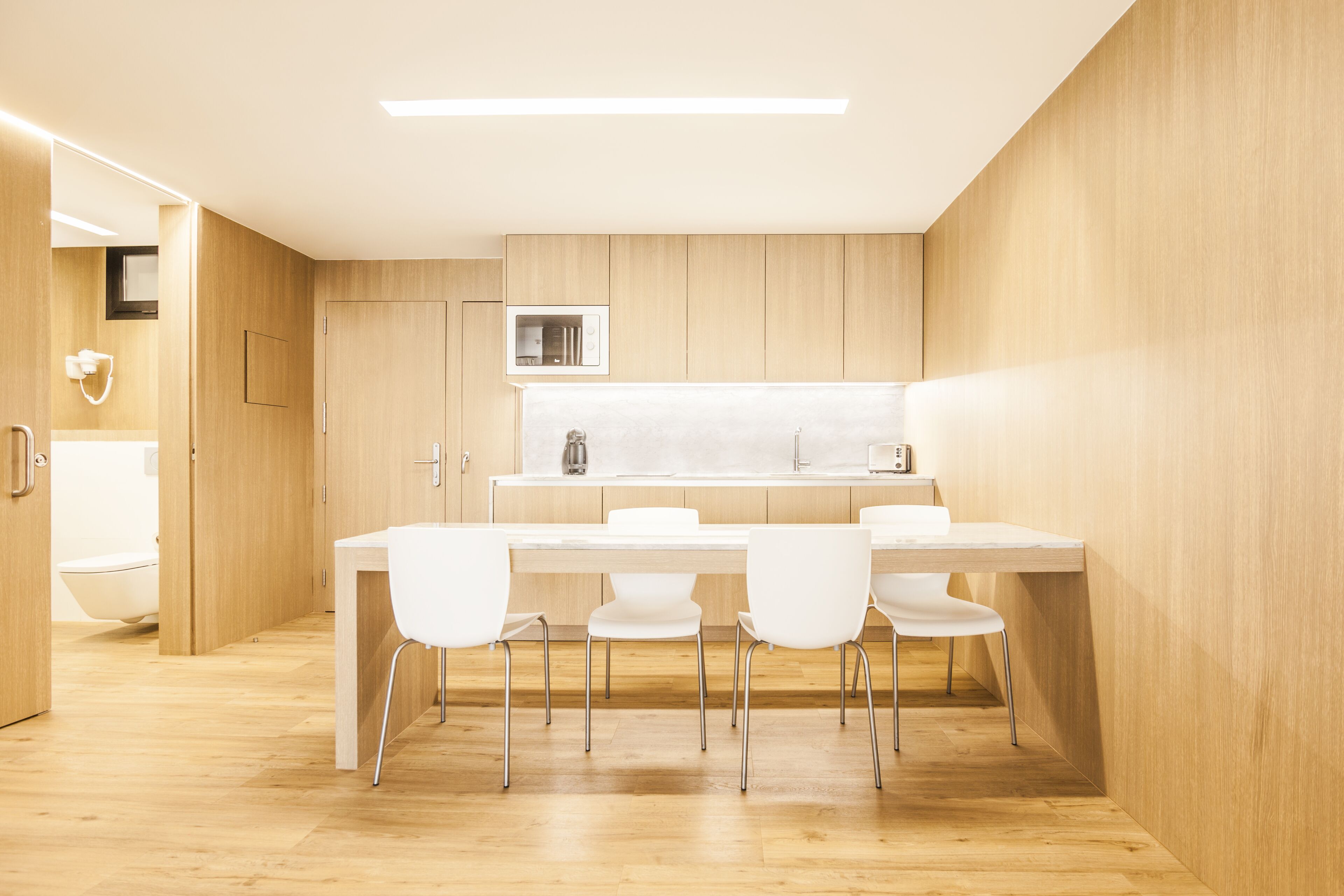 A modern kitchen with a wooden countertop, white chairs, and a built-in microwave.
