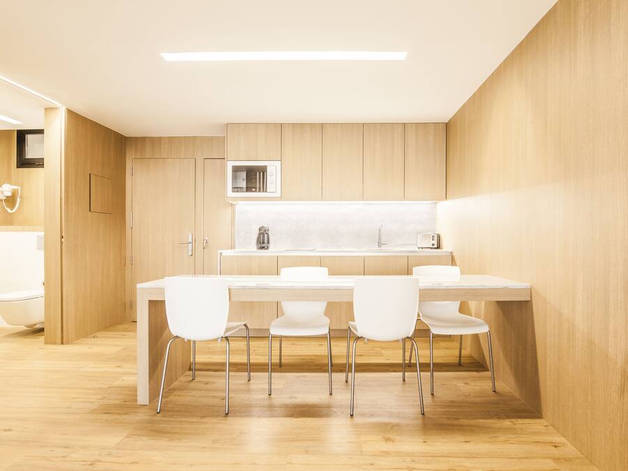 A modern kitchen with a wooden countertop, white chairs, and a built-in microwave.