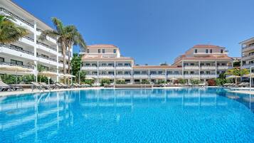 Ein Hotel mit großem Schwimmbecken, mehreren Balkonen und Palmen.