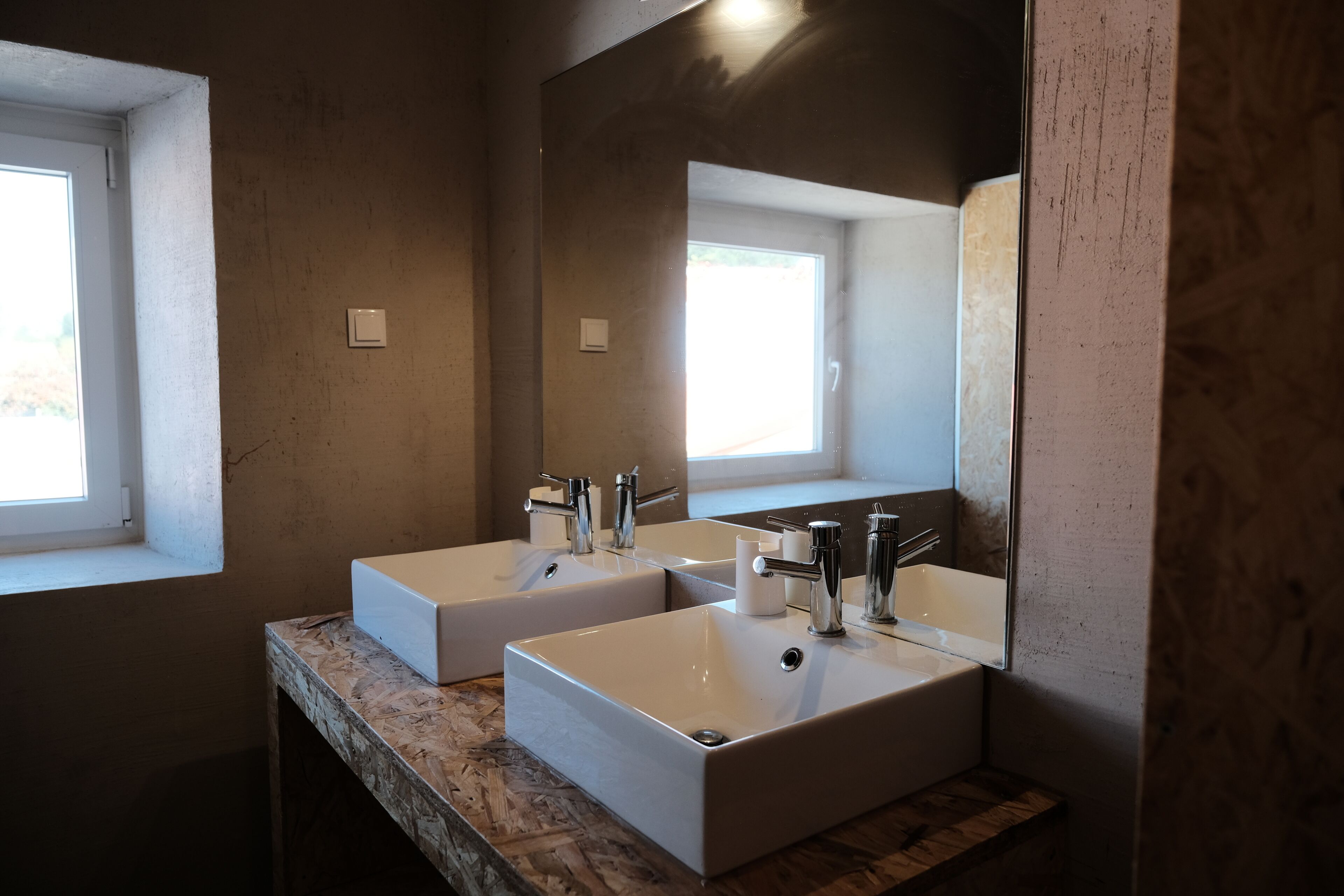 A bathroom with two white sinks, a large mirror, and a window providing natural light.