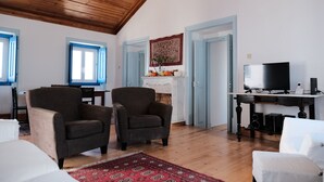 A spacious living room with wooden ceiling, two armchairs, a white sofa, a red rug, a fireplace with a decorative piece, and a TV on a wooden stand. - Azoia 10 (Santarém)