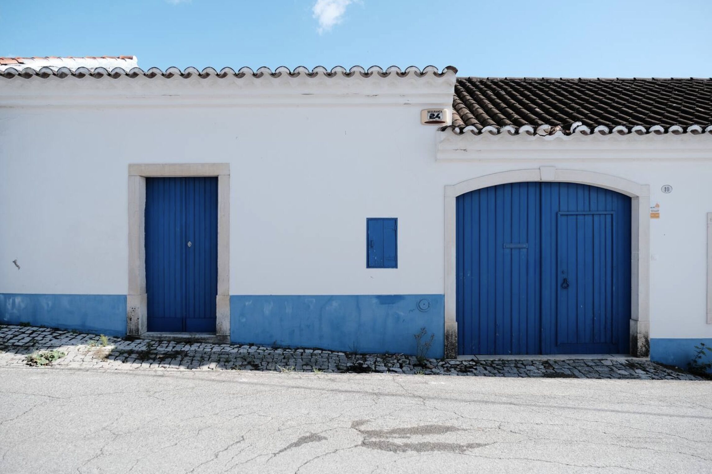 A building with two blue doors, a tiled roof, and a cobblestone pathway.