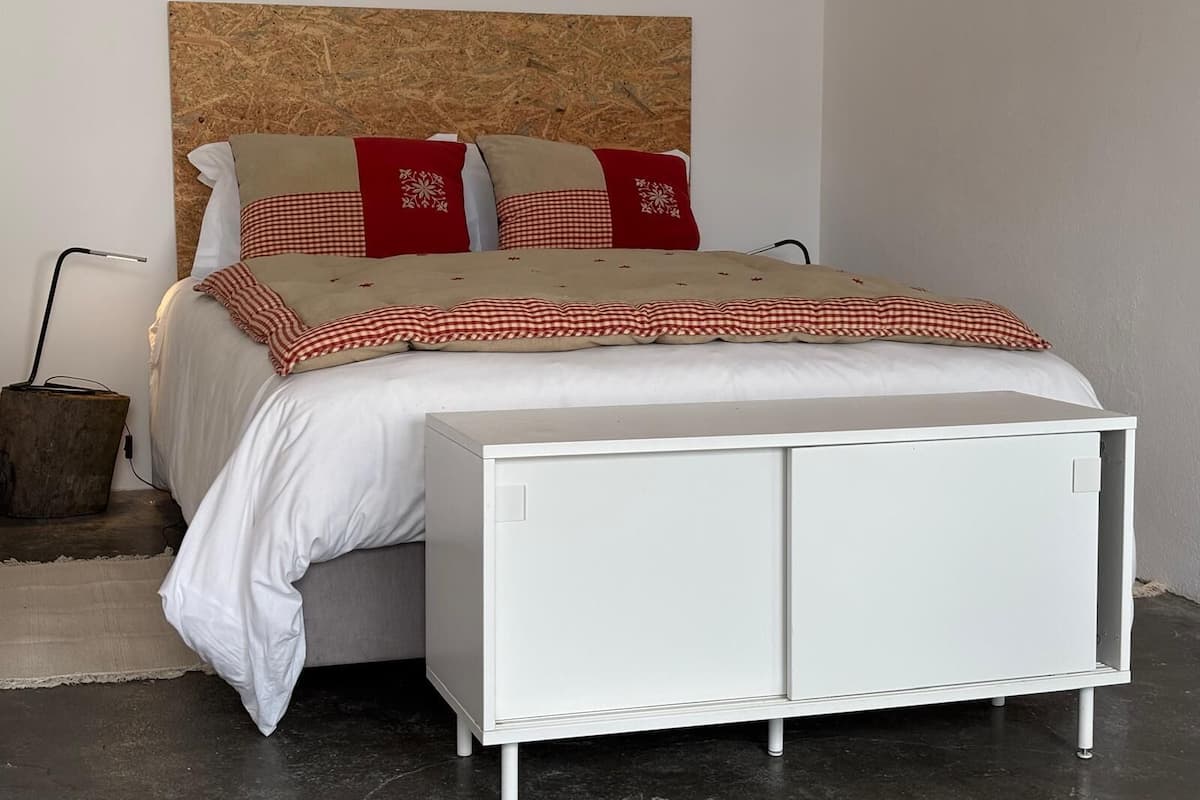 A bedroom with a bed, a bedside table, a lamp, and a wall-mounted artwork.