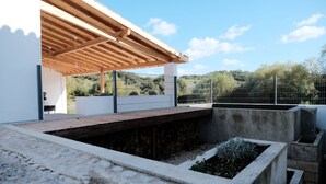 A modern outdoor patio area with a wooden pergola, stone flooring, and a concrete planter with plants. - Azoia 10 (Santarém)
