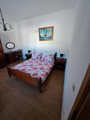 A bedroom with a wooden bed, a desk, a chair, a dresser, a painting, and a lamp.