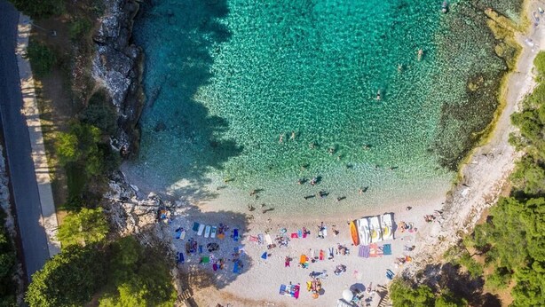 An aerial view of a beach with clear turquoise water, a sandy shore, and a few people and umbrellas. - Apartment for five people with a terrace (Pula)