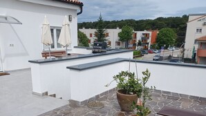 A rooftop terrace with stone flooring, two potted plants, a barbecue grill, and outdoor seating with umbrellas. - Apartment for five people with a terrace (Pula)