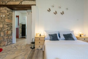 Un dormitorio con pared de piedra, una cama con dos almohadas, una mesita de noche con lámpara y suelo de madera.