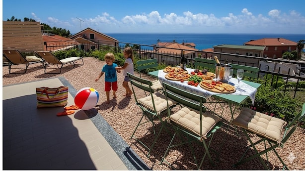 Una terraza con mesas al aire libre, una mesa con comida y vista al mar.