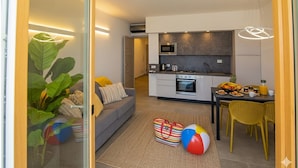 Una sala de estar moderna con un sofá, un comedor con sillas amarillas y una cocina con microondas y estufa.