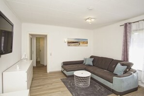 A modern living room with a sectional sofa, a small round table, and a flat-screen TV mounted on the wall.