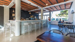Un área de bar amplia con una barra larga, taburetes de metal y techo de madera.