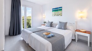 Habitación de hotel con dos camas, un balcón, un cuadro y una mesita de noche con lámpara.