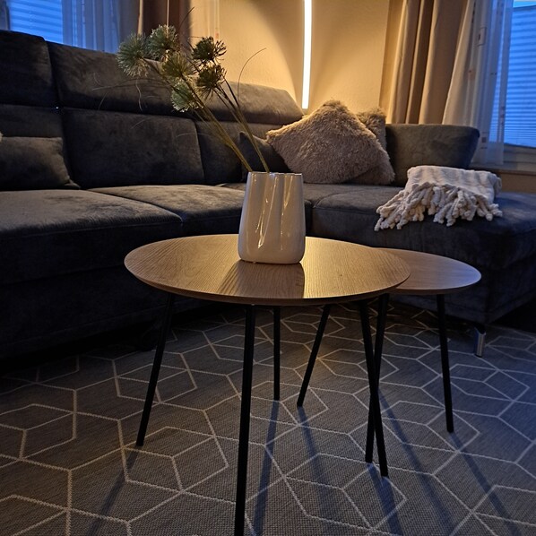A living room with a dark sofa, a round wooden coffee table with a white vase, and a geometric patterned rug. - Eigene Wohnung mit Garten und Terrasse am Dümmer See (Lembruch)
