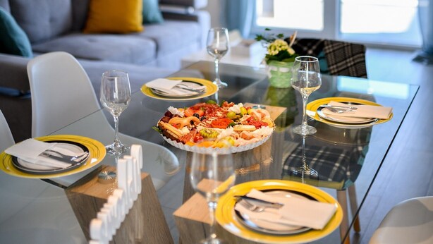 Un comedor moderno con mesa de vidrio, lámparas colgantes de metal y vistas a una piscina a través de amplios ventanales.