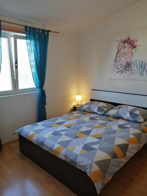 A bedroom with a bed, curtains, a nightstand, a lamp, and a wall painting.